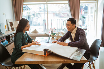 beautifull shopkeeper helping the asian customer choosing the window treatments from the catalogue book inside the curtain shop