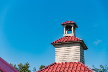 Architectural detail: a small bell tower with a red roof. The tower is made of wood, showing signs of weathering and age. A bell hangs in the open top of the tower.