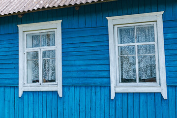 Close-up of a wooden building with windows. The building is painted in a bright, vibrant blue. The windows are framed in white, providing a stark contrast to the blue background.