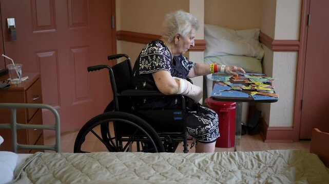 An elderly woman with a bandaged arm sits at a table, carefully placing puzzle pieces together. The puzzle depicts a map of the United States. She appears focused and determined, engrossed in the tas