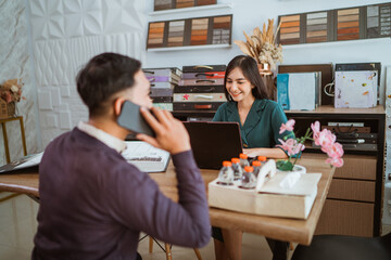 asian male customer calling on phone while choosing the window treatments features helped by the beautiful female shopkeeper