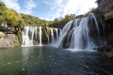 Obraz premium Majestic waterfalls cascade into a tranquil pool surrounded by lush greenery in autumn