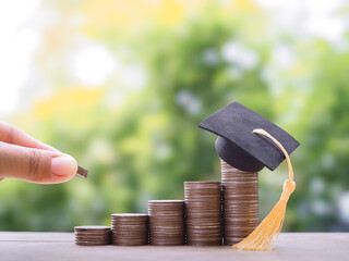 Close up of hand putting coins in stack of coins with graduation hat. The concept of saving money...