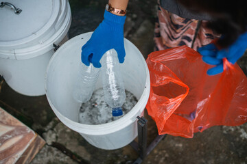 crop and high angle view female hand wearing gloves putting plastic bottle into trash can