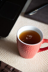 The mug is placed on a light-colored woven placemat, and a laptop is visible in the blurred background, suggesting a work or study setup.