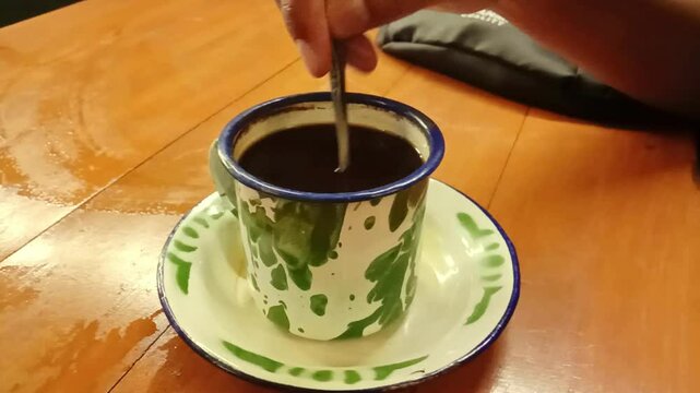 Close-up view of a man stirring black coffee with a spoon. Suitable for content related to drinks, coffee, relaxation and lifestyle. Ideal for cafe promotions or coffee advertising visual materials