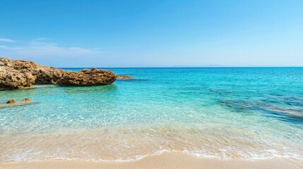 Obraz premium Scenic beach with clear water and rocky coastline under a vibrant blue sky.