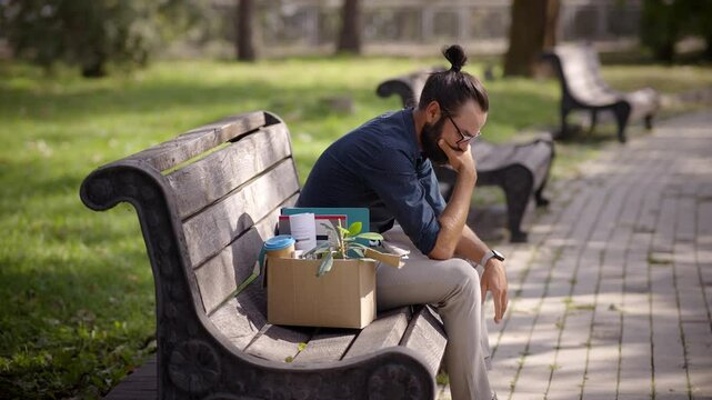Man contemplating lost job sitting on park bench with box 