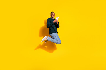 Obraz premium Full body photo of nice young male jump hold device wear trendy green outfit isolated on yellow color background