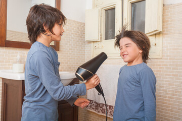 Two young boys are drying their hair with a blow dryer