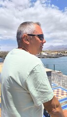 Fototapeta premium Portrait of young adult man alone sad and serious, profile of man with sea view.Portrait alone sad looking at sea and thinking,outdoor photo of profile of dreamy man.charming man looking at the sea.