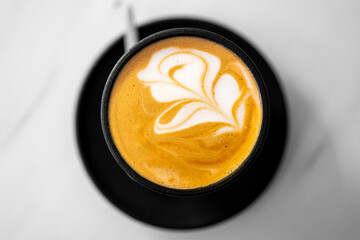 Top view of a cup of coffee with intricate latte art on a saucer. dark cup contrasts with the...