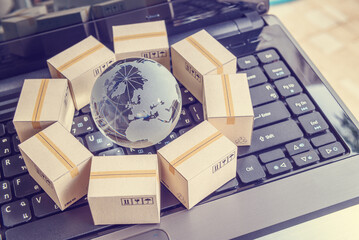 International freight or shipping service for online shopping or ecommerce concept : Paper boxes or carton put in circle around a clear crystal globe with world map on a computer notebook keyboard.