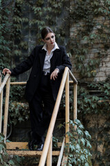 Portrait of stylish and attractive Caucasian young brunette woman in a suit, posing outdoors on iron stairs. Beauty, fashion, style. Well-dressed model.