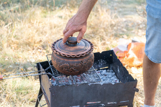 Clay pot with food on the grill. Cooking food on a fire outside. Camping outdoor. Sheff hand