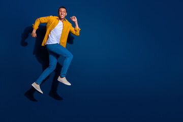 Obraz premium Full body length photo of attractive sporty man short hair wearing jeans and shirt running fast isolated on dark blue color background