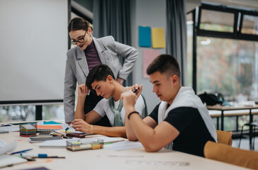 Students engaged in group study while being supervised by a teacher in a modern classroom. The environment is collaborative, with focus on education and teamwork.