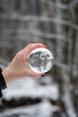 Naklejka premium Hand holding a glass ball, trees with snow reflected in it