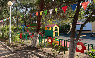 Colorful children's playground in a kindergarten setting with play structures and tables surrounded by trees