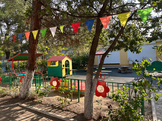 Colorful children's playground in a kindergarten setting with play structures and tables surrounded...