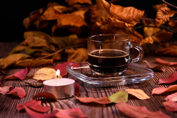 Cup of coffee, coffee beans on a saucer on a table with autumn leaves and candles. Romantic atmosphere.