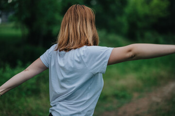 A young woman stands with outstretched arms, embracing the tranquil nature around her in a lush green park.