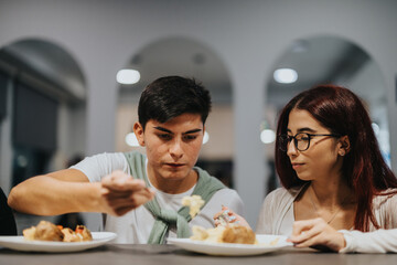 Two high school students are seated at a table in a cafeteria, sharing a casual meal. The setting...