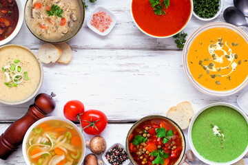 Assorted delicious homemade soups. Top down view frame on a white wood background. Warm and cozy food concept.