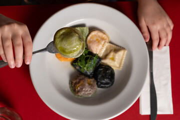 A vibrant plate of sorrentinos and ravioli showcasing different flavors and colors. The dish includes green, orange, black, and white pasta varieties, drizzled with olive oil and garnished with fresh 