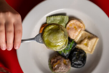 A vibrant plate of sorrentinos and ravioli showcasing different flavors and colors. The dish includes green, orange, black, and white pasta varieties, drizzled with olive oil and garnished with fresh 