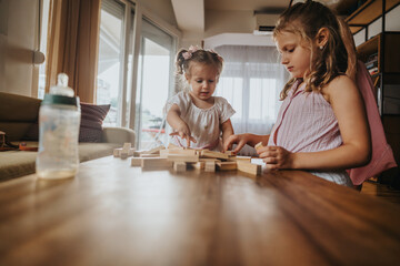 Two young children playing with wooden blocks inside a cozy home, enjoying family time together in...