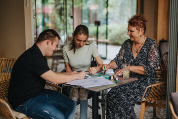 Elderly woman helps a young man with Down syndrome and a girl in a wheelchair engage in a creative...