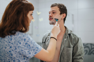 A couple getting ready for a night out, with the woman helping the man shave in the bathroom. Captures a moment of intimacy and preparation.