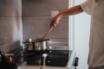 A person stirs pasta in a pot on a modern stove, showcasing home cooking and culinary skills in a cozy kitchen setting.