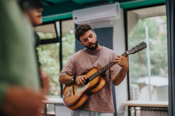 A young man is focused on playing the guitar in a well-lit, modern classroom setting, conveying a sense of creativity and learning in music education.