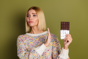 Young woman in colorful knitwear refusing chocolate bar against khaki background for shopping or...