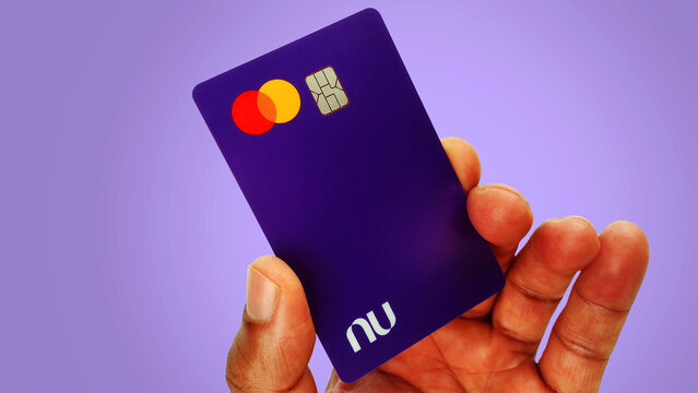 Black male hand holding Nubank visa credit card on the white background with copy space. Nubank chip card. Itabira - Brazil. October 08, 2024.