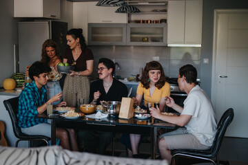 A group of friends enjoying a relaxed meal in a modern kitchen, sharing food and laughter around a table. The atmosphere is warm and inviting.