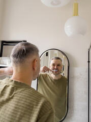 A man is brushing his teeth in a modern bathroom, looking at his reflection in the mirror with a smile.