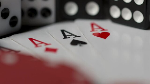Close up of poker chips and set of aces playing cards with black and white roll dices in the background on a black table top with smooth sliding and panning motion