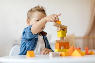 Fotobehang Lego Early development concept. A child focused on building a tower with colorful wooden blocks in a well-lit playroom, fostering creativity and fine motor skills through play.  © Anastasiya