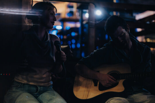 A singer and guitarist perform an intimate acoustic set in a dimly lit setting, exuding a soulful and serene atmosphere. Perfect for themes of music, performances, and artistic expression.