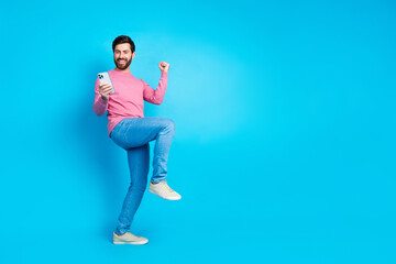 Joyful man celebrating success in fashion with casual wear while holding smartphone against vibrant...