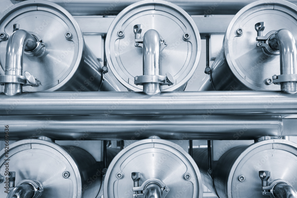 Poster Machine for the production of dairy products with a series of metal stainless steel cylinders and pipes with silver trim. cylinders are connected to each other and appear to be part of a larger system