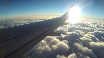 Obraz premium Airplane wing over clouds with sun shining brightly.