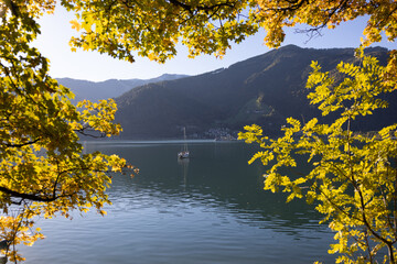 Autumn in Zell am See, Austria. Colourful nature landscape with a sailing boat and picturesque trees during the sunset