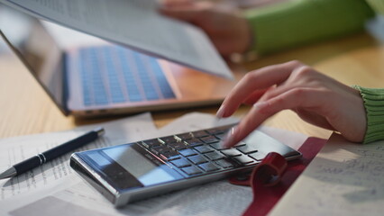 Accountant hand pressing calculator buttons working at wooden table closeup