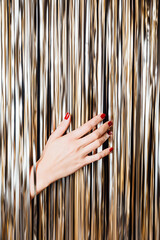 Woman hand touch Golden foil tinsel strips. Creative festive background for christmas, new year,...