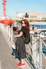 A mother with a two-year-old child, a girl, on the embankment in the Bay pier with ships in Kaliningrad