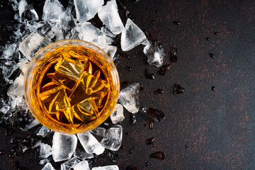 Glass of whiskey with ice cubes on black background. As whiskey is poured from the bottle into the...